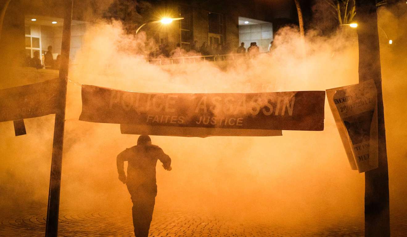 A man runs away from tear gas launched by riot police next to a banner reading, Police murderer, Do justice, during a protest in front of the police headquarters in the 19th arrondissement of Paris on Tuesday. Photo: AFP