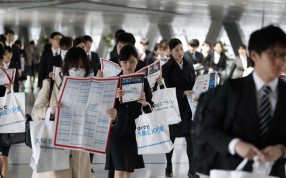 University students hold floor maps as they walk through a job fair in Tokyo. Many younger workers in Japan accept taking non-regular contract jobs with longer hours due to their lack of experience. Photo. Bloomberg