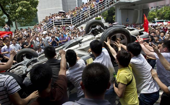 A crowd overturns a Japanese-brand police car in Shenzhen. Photo: Reuters