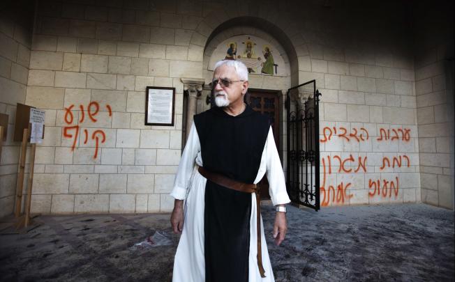 A Trappist monk walks between graffiti which was sprayed on the wall of the Christian Catholic Latrun monastery between Jerusalem and Tel Aviv on Tuesday after unknown people set the monastery’s door ablaze and vandalised its wall. Photo: AFP 