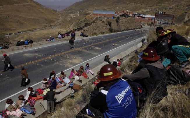 Miners sit along a road where they placed stones to block traffic on the outskirts of La Paz, Bolivia, on Tuesday. Photo: AP