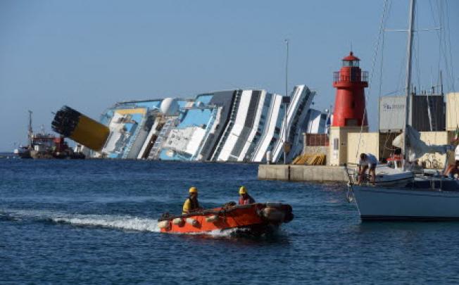 Italian salvage members entering the harbour with a view of the stranded Costa Concordia cruise ship in the background, near the Giglio Porto. Photo: AFP