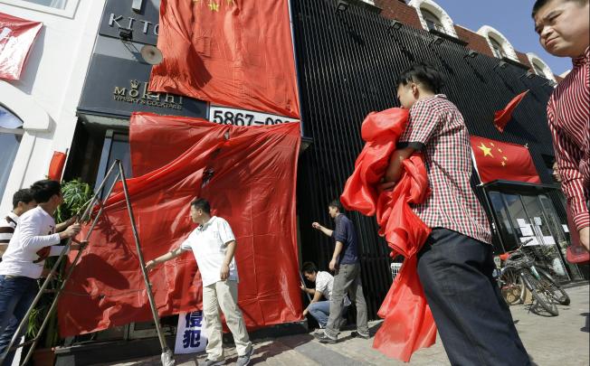 Protesters in Beijing target a Japanese restaurant, covering its sign with the Chinese flag on Monday. Photo: AP