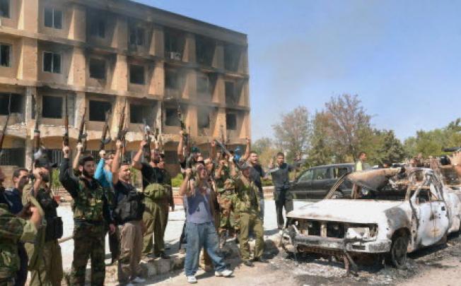 Syrian army soldiers raise their guns outside a research centre following clashes with rebels in Aleppo. At least 30 civilians were reported killed on Thursday in a massive explosion in northeast Syria.