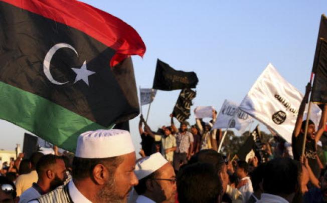 Libyans, foreground, pass by a demonstration by Ansar al-Shariah and other Islamic militias, background, as they march against the militias in Benghazi on Friday. Photo: AP