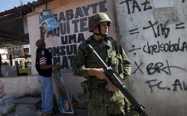 An Electoral Tribune worker removes illegal campaign banners while a Brazilian soldier patrols the Fogo Cruzado slum in Rio de Janeiro on Monday. Photo: AP