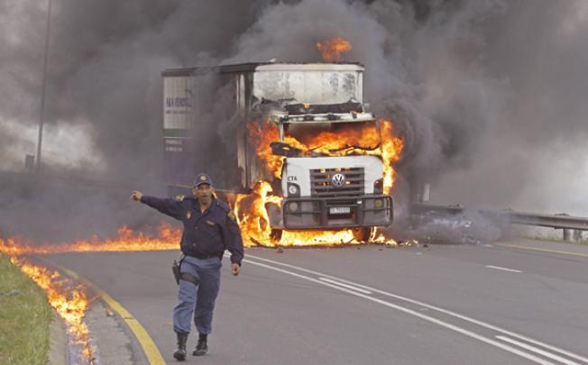 A police man reacts as flames and smoke emerge from a truck after it was set alight by striking truck drivers, near Cape Town, on Wednesday. Photo: AP