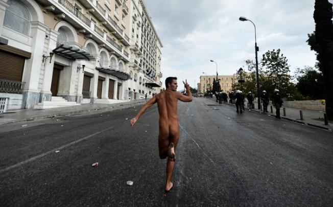A naked demonstrator flashes the victory sign while running in Athens during a demonstration against the vist of the German Chancellor Angela Merkel on Tuesday. Photo: AFP