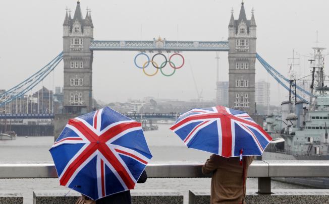 Two tourists stand under Union flag umbrellas as they take pictures of the Tower Bridge on July 6, 2012. Photo: Reuters 