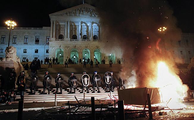 Riot police guard the parliament building in Lisbon near a fire set by protesters against the austerity measures on Monday. Photo: AP