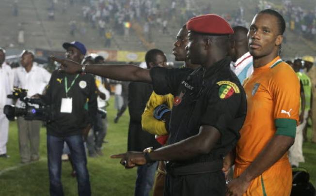 A Senegalese policeman stands in front of Ivory Coast captain Didier Drogba, after rioting Senegal fans caused Ivory Coast's African Cup of Nations qualifier against Senegal to be suspended. Photo: AP