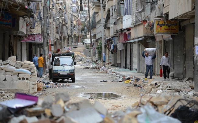 Civilians carry belongings down a street strewn with debris in Aleppo. Photo: AFP