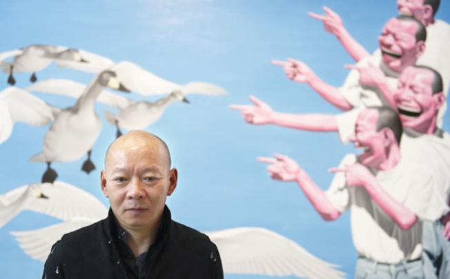 Yue Minjun poses in front of one of his paintings displayed in an exhibition entitled "L'ombre d'un fou rire" (The shadow of a laugh) in Paris on Tuesday. Photo: AFP