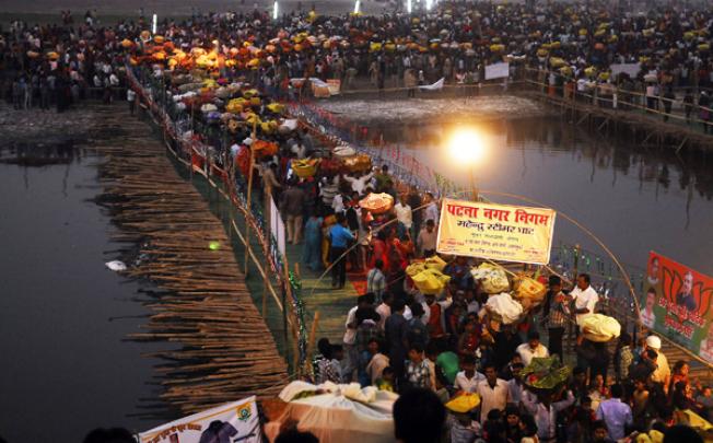 Indian Hindu devotees cross a bamboo bridge as they gather to pay homage to the setting sun on the banks of the Ganges River on Monday. Photo: AFP