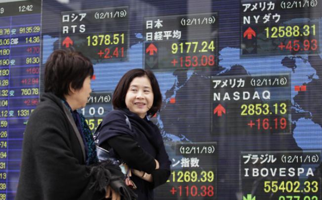 Women walk past an electronic stock indicator in Tokyo on Monday as the yen's recent weakness helped boost Japan's Nikkei 225. Photo: AP Photo