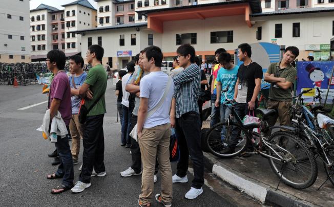 Foreign workers wait for their transportation to work outside their dormitory in Singapore on Monday. Photo: AFP 