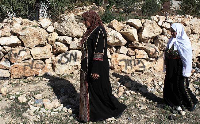Palestinian women walk past graffiti sprayed by Israeli settlers in the village of Khirbet al-Assia in the Israeli occupied West Bank. Photo: AFP 