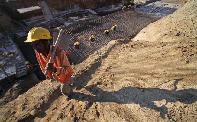 A worker walks with a spade as others lay iron bars for a bridge under construction in the Jammu-Srinagar highway. Photo: AP