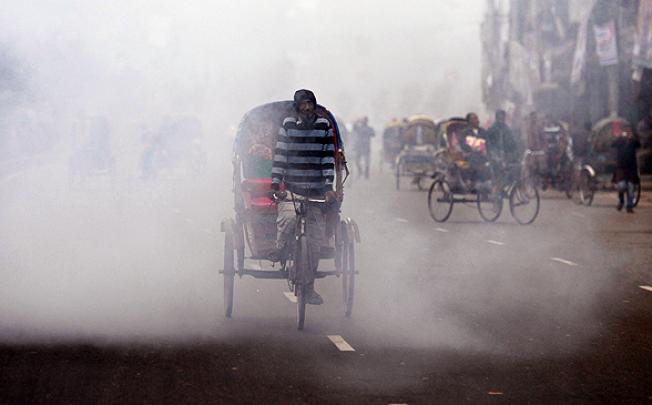 A Bangladeshi rickshaw driver cycles past the cloud of a smoke bomb during a nationwide strike in Dhaka on Tuesday. Photo: AFP