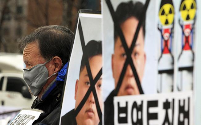 A South Korean protester sits near defaced portraits of North Korean leader Kim Jong-un during a rally denouncing North Korea's rocket launch in Seoul on Thursday. Photo: AP