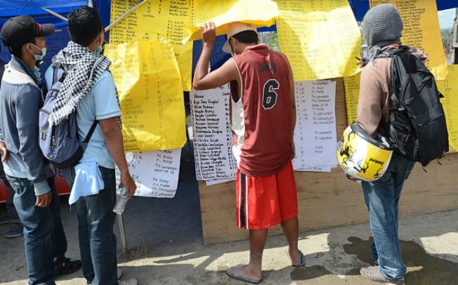 Residents look through lists of missing people posted in New Bataan. Photo: AFP