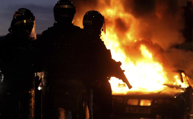 Riot police stand next to a burned out car on Saturday night, after Loyalist protesters attacked police lines, in east Belfast, Northern Ireland. Photo: AP