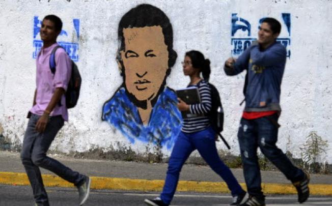 Youngsters walk in front of a banner of Venezuelan President Hugo Chavez in Caracas. Photo: AFP