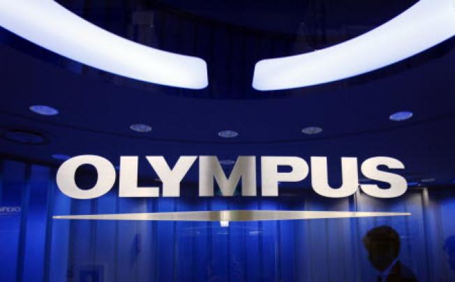 A man passes behind a logo of Japan's Olympus Corp at the company headquarters in Tokyo. Photo: Reuters