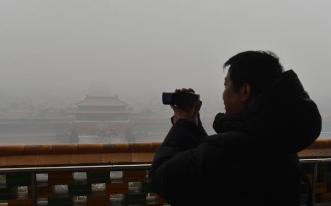 A Chinese tourist takes photos of the Forbidden City from the historic Jingshan Park as smog continues to shroud Beijing. Photo: AFP