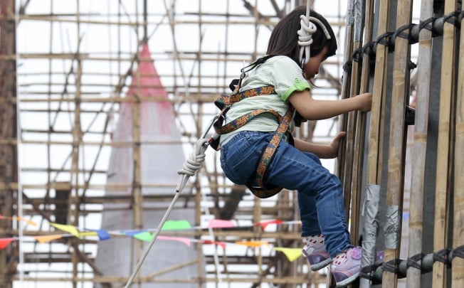 Four-year-old Wong Yuen-yan scales the bun tower outside Pak Tai Temple on Cheung Chau island yesterday. The event allowed children to climb the metal tower to be used for this Saturday's bun-scrambling contest during the island's popular Bun Festival. The plucky little girl managed to climb to the top of the structure, which was about 18 metres high, and won the applause of onlookers. Photo: Dickson Lee