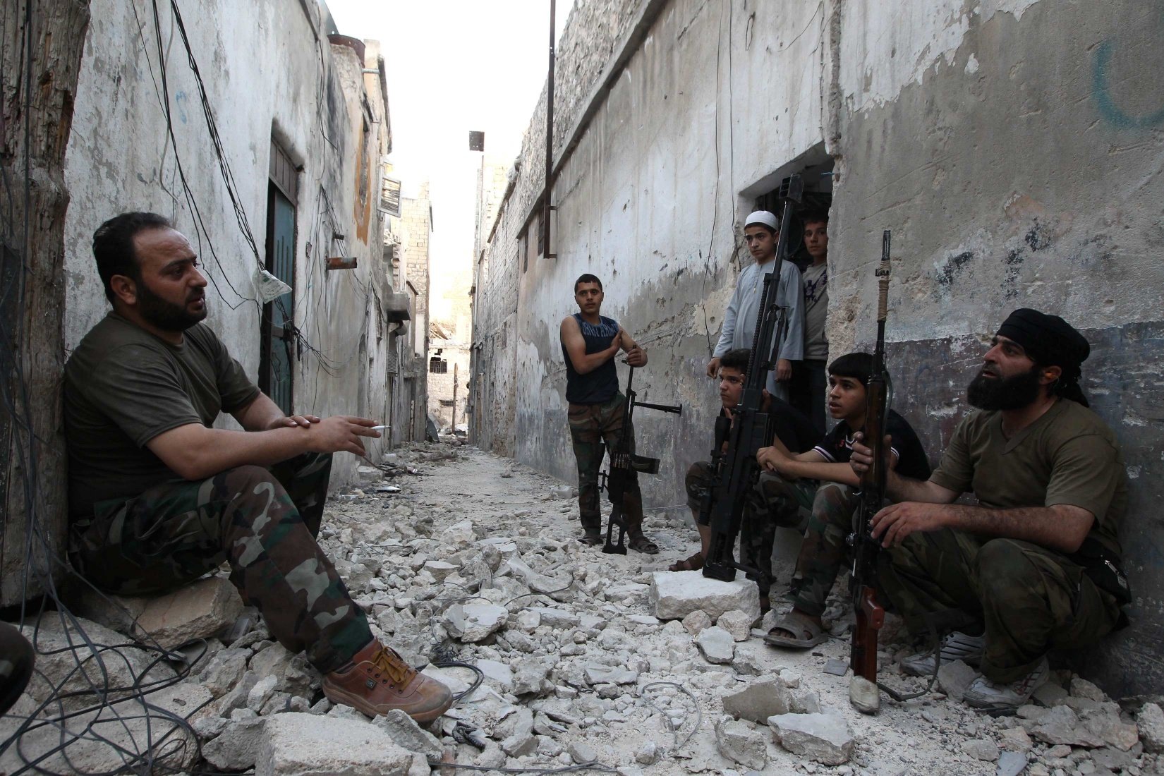 Members of the Free Syrian Army talk as they sit with their weapons in a damaged street in Aleppo's Karm al-Jabal district. A missile strike near Aleppo has killed 26. Photo: Reuters
