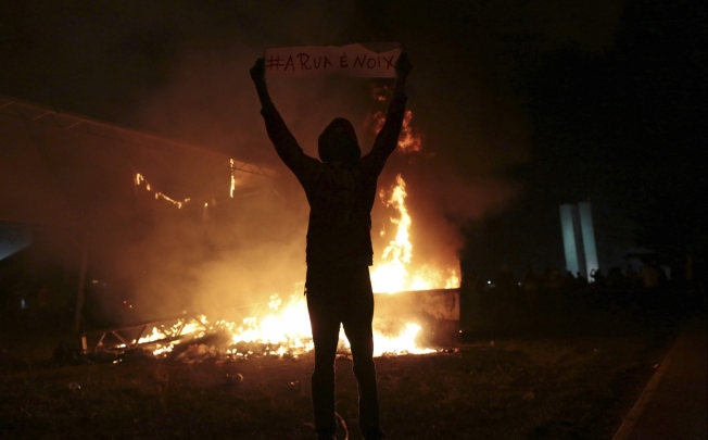 A demonstrator holds a sign next to a fire during a protest against the Confederations Cup and the government in Brasilia. Photo: Reuters