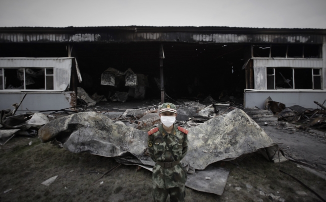 A paramilitary policeman wearing a mask stands guard in front of the burnt-out site of a poultry slaughterhouse in Dehui. Photo: Reuters