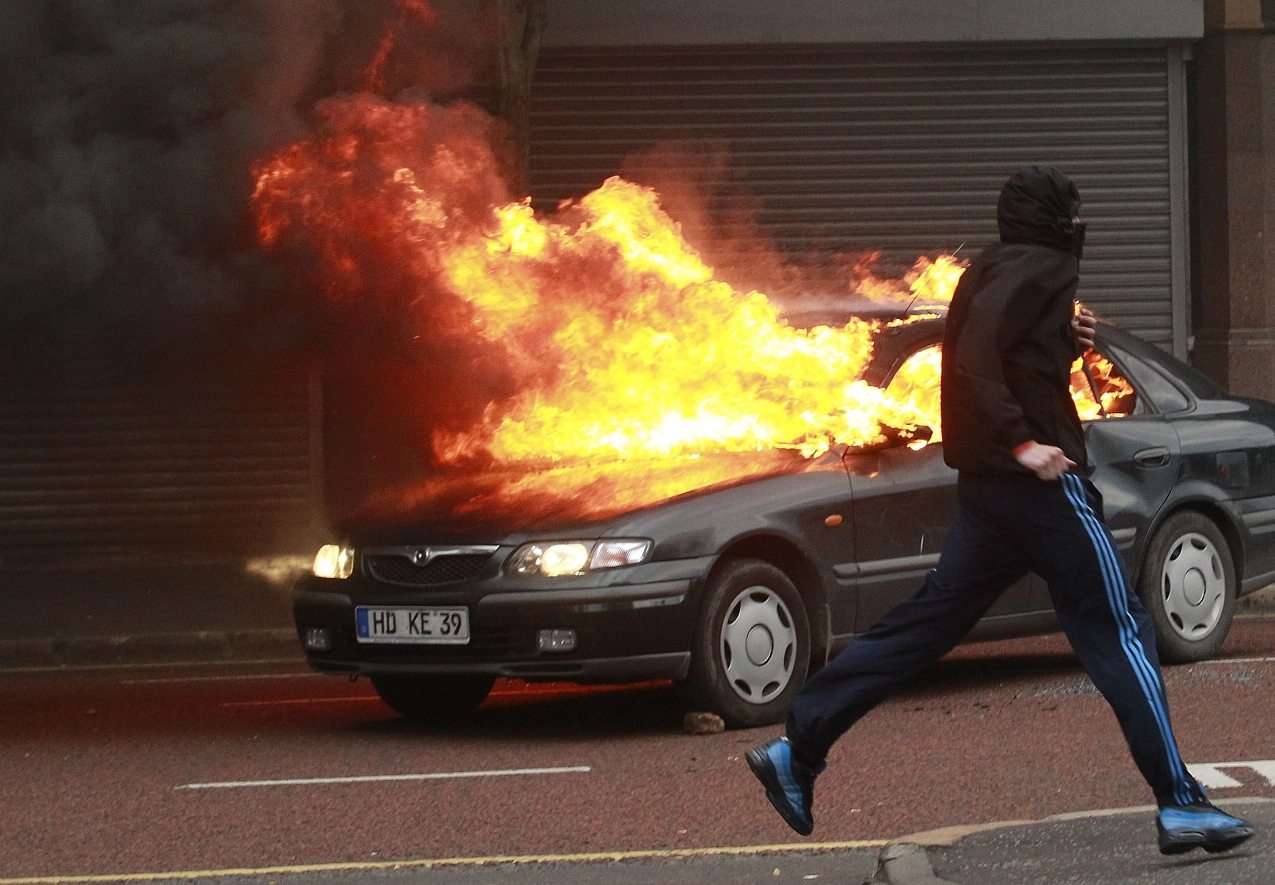 A Loyalist protester runs past a burning car during rioting in the centre of Belfast on Northern Ireland, Friday. Photo: AP