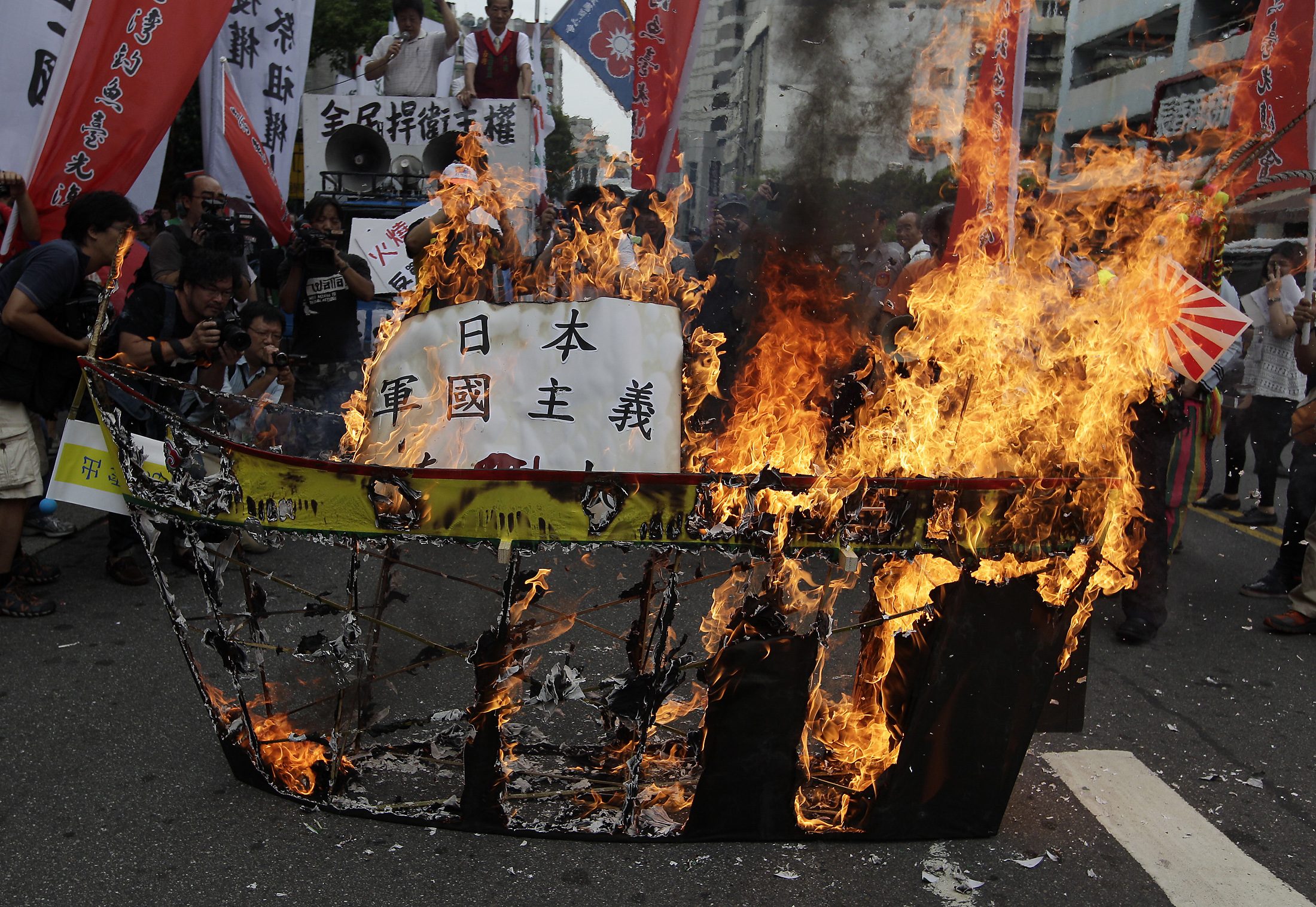 Activists burn a paper ship symbolising Japan's helicopter destroyer Izumo during an anti-Japan protest in front of the Japan Interchange Association in Taipei