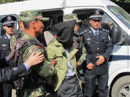 Farmer Ma Yongdong (hooded) is taken to the scene of the crime in Pengyang county after he was arrested in a distant town following the stabbing attack. Photo: Xinhua
