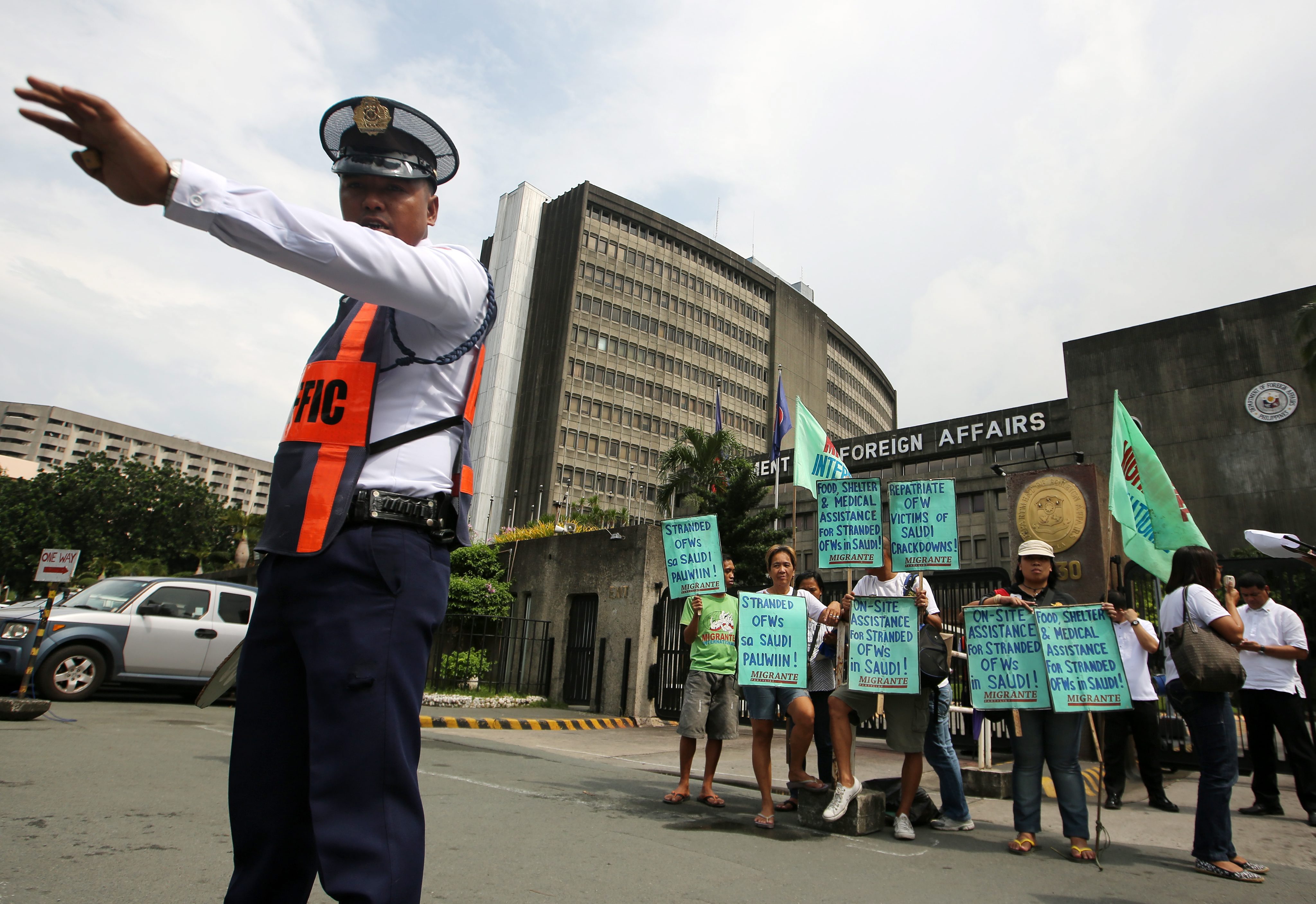 A Filipino security officer directs traffic as protesters hold banners outside the Department of Foreign Affairs. Photo: EPA