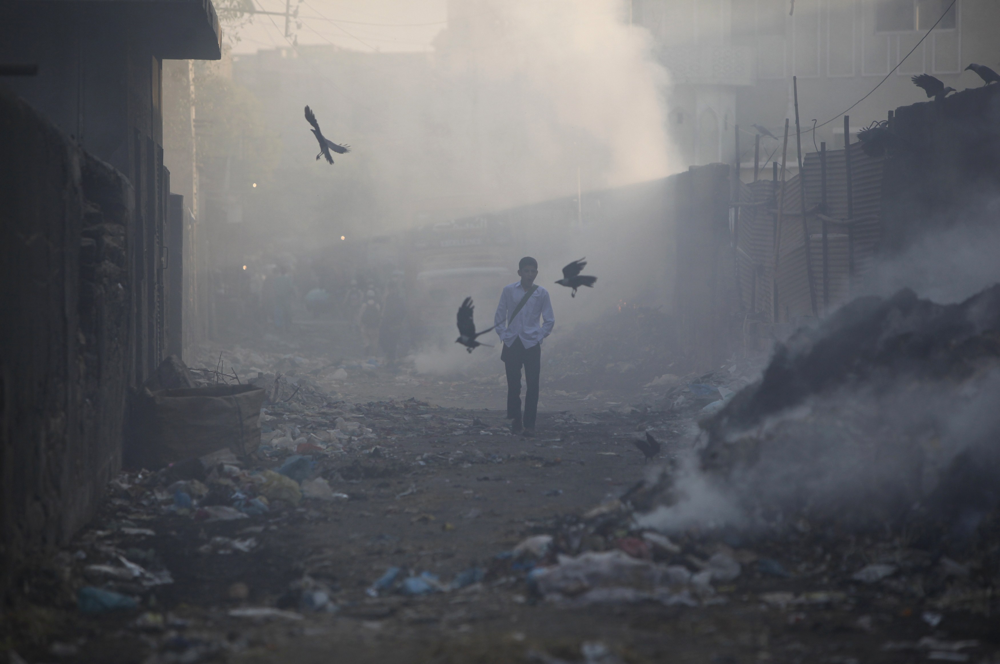 A boy walks through alley littered with pile of smouldering waste, while heading to school during early hours of the morning in Karachi. Photo: REUTERS