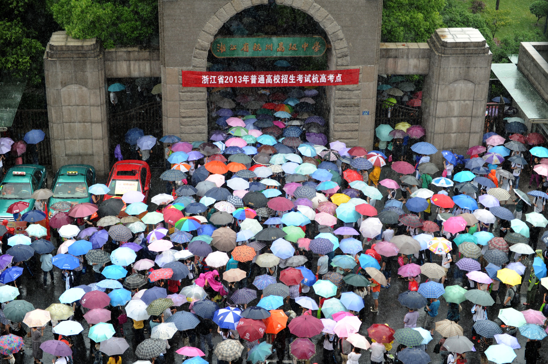 Parents holding umbrellas wait in rain as their children taking the national college entrance exam at the Hangzhou High School in Hangzhou, Zhejiang Province, June 7, 2013. Photo: Xinhua