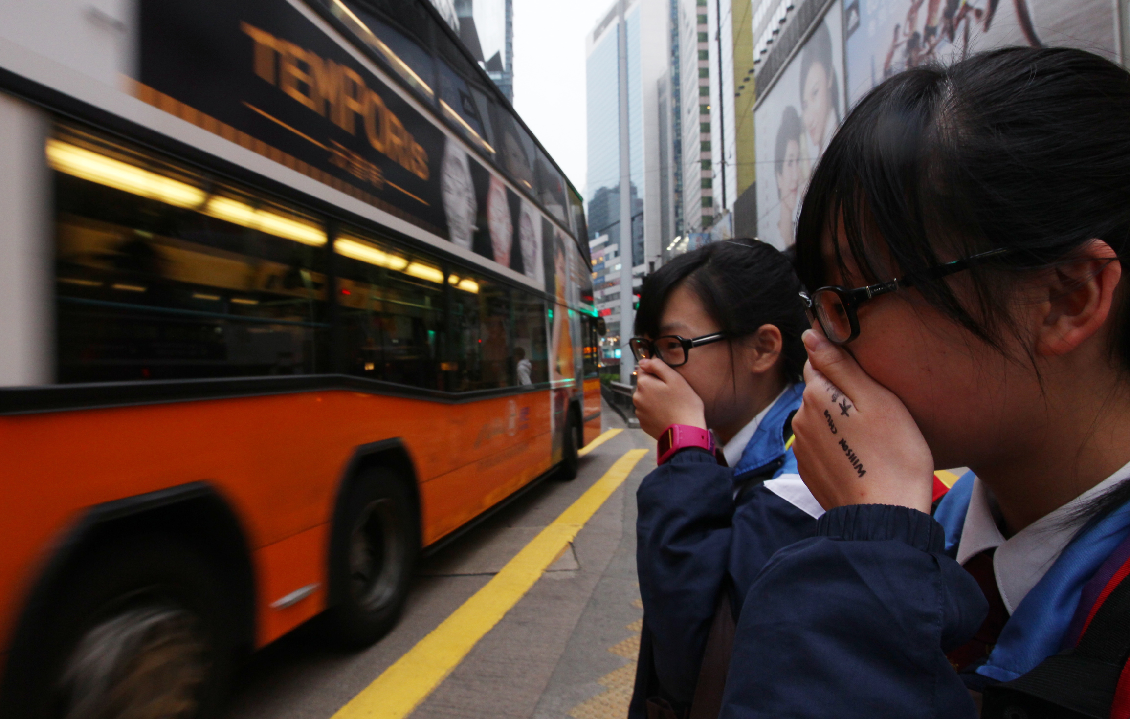 Students cover their noses to avoid emissions from vehicles as they cross Yee Wo Street in Causeway Bay. Photo: Nora Tam