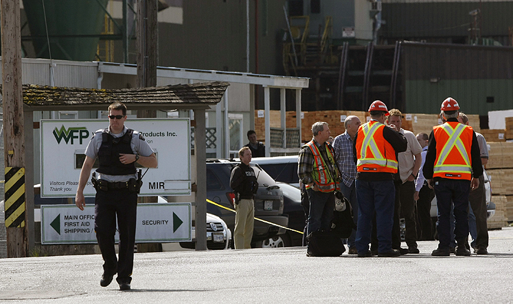 Mill workers talk as a police officer walks away following the shooting at Western Forest Products in Nanaimo, British Columbia on Wednesday. Photo: AP