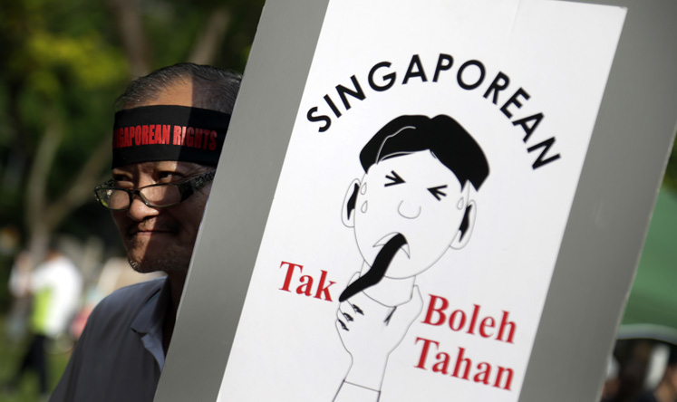 A man carries a poster which translates from the Malay language as "Singaporean can't take it!" at a May 1 protest calling for tighter curbs on the influx of foreigners into the city state. Photo: AP
