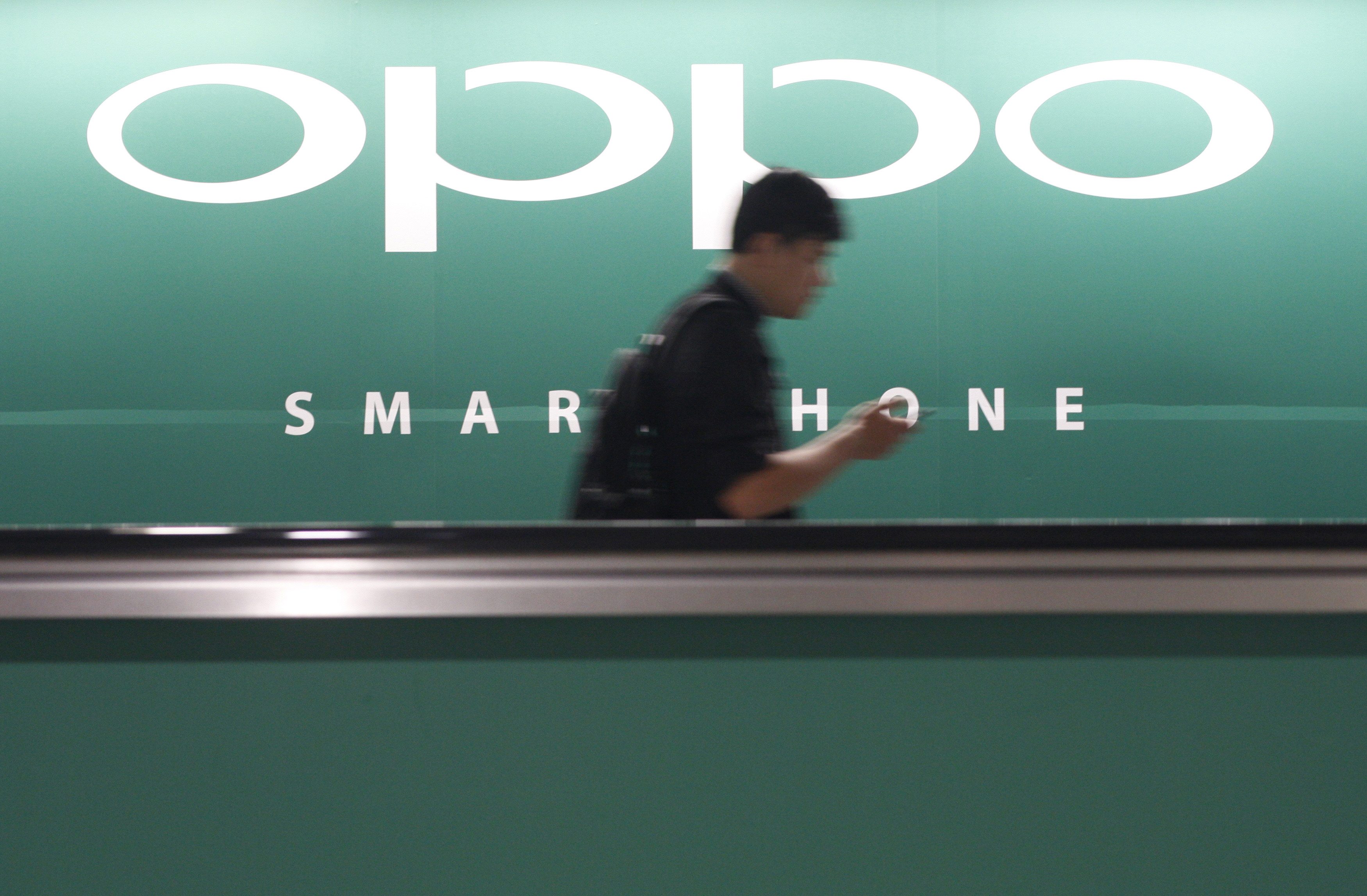 A commuter using his mobile phone passes an advertisement of Chinese smartphone maker Oppo at a train station in Singapore. Photo: Reuters
