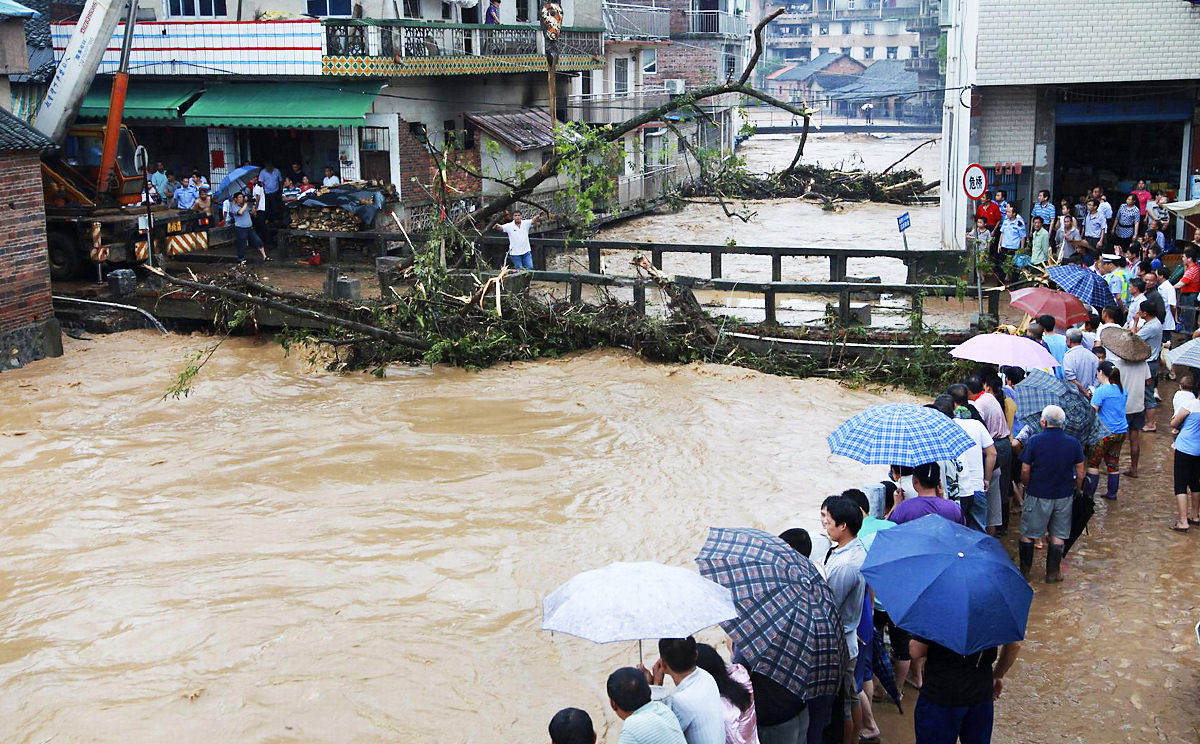 Residents look on as debris from heavy rains gathers at a bridge over a flooded river in Shitang, Guangxi. Photo: Reuters