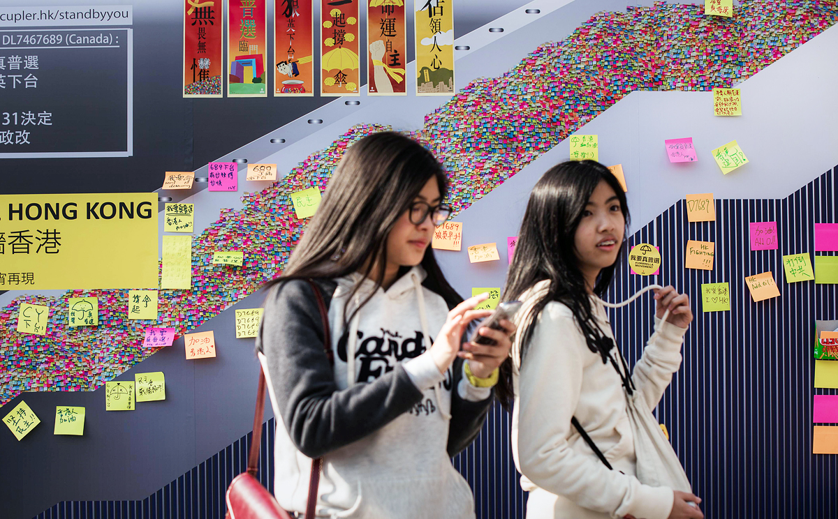 Two girls walk past a billboard depicting the "Lennon wall" during the Occupy Central movement. The city has been plagued by a culture of suspicion that divides its people into polar opposites and sometimes blinds them to common sense. Photo: AFP