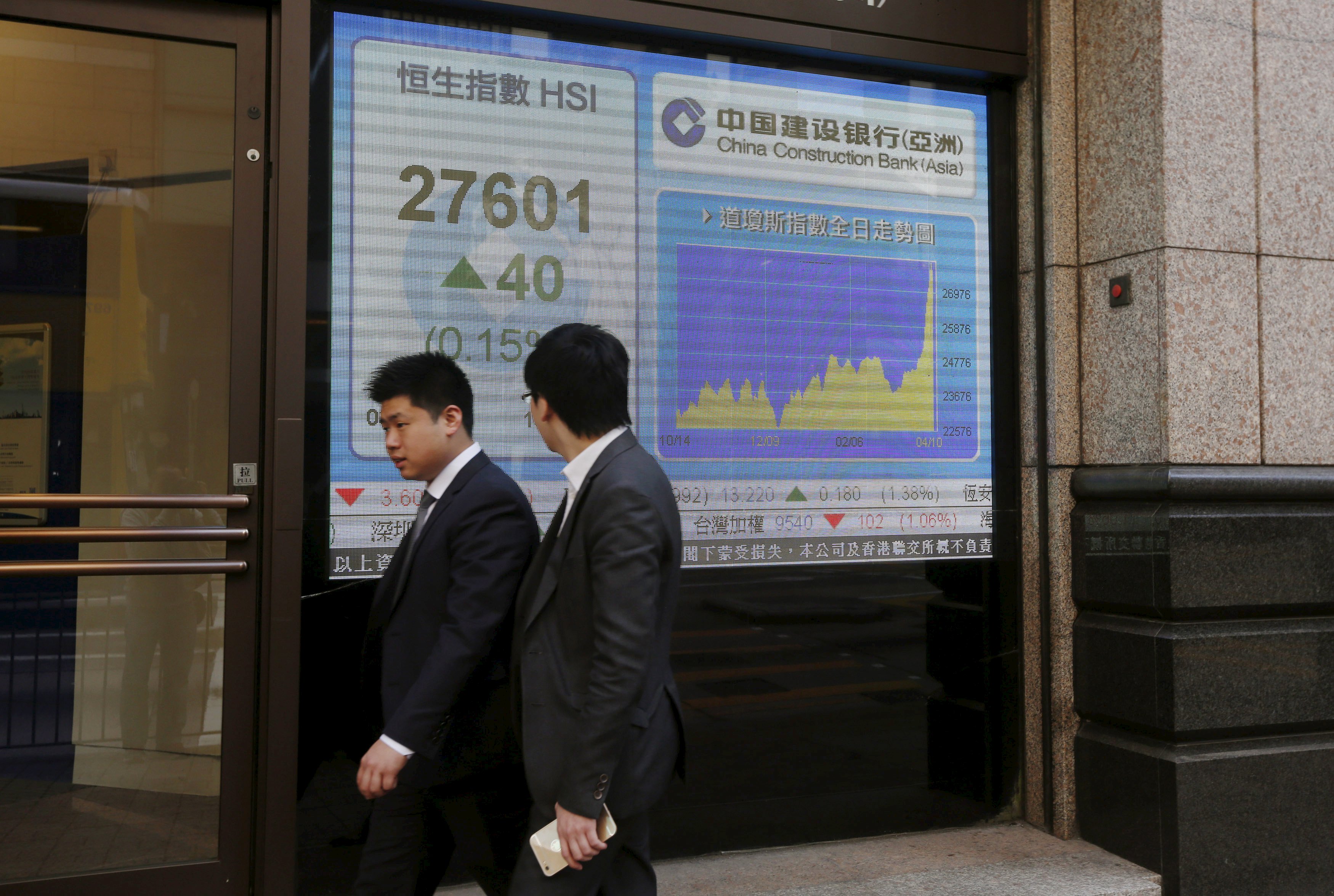Businessmen walk past an electronic board showing the Hang Seng index which surged at the start on Monday to hit fresh highs along with the Shanghai index in China. Photo: Reuters