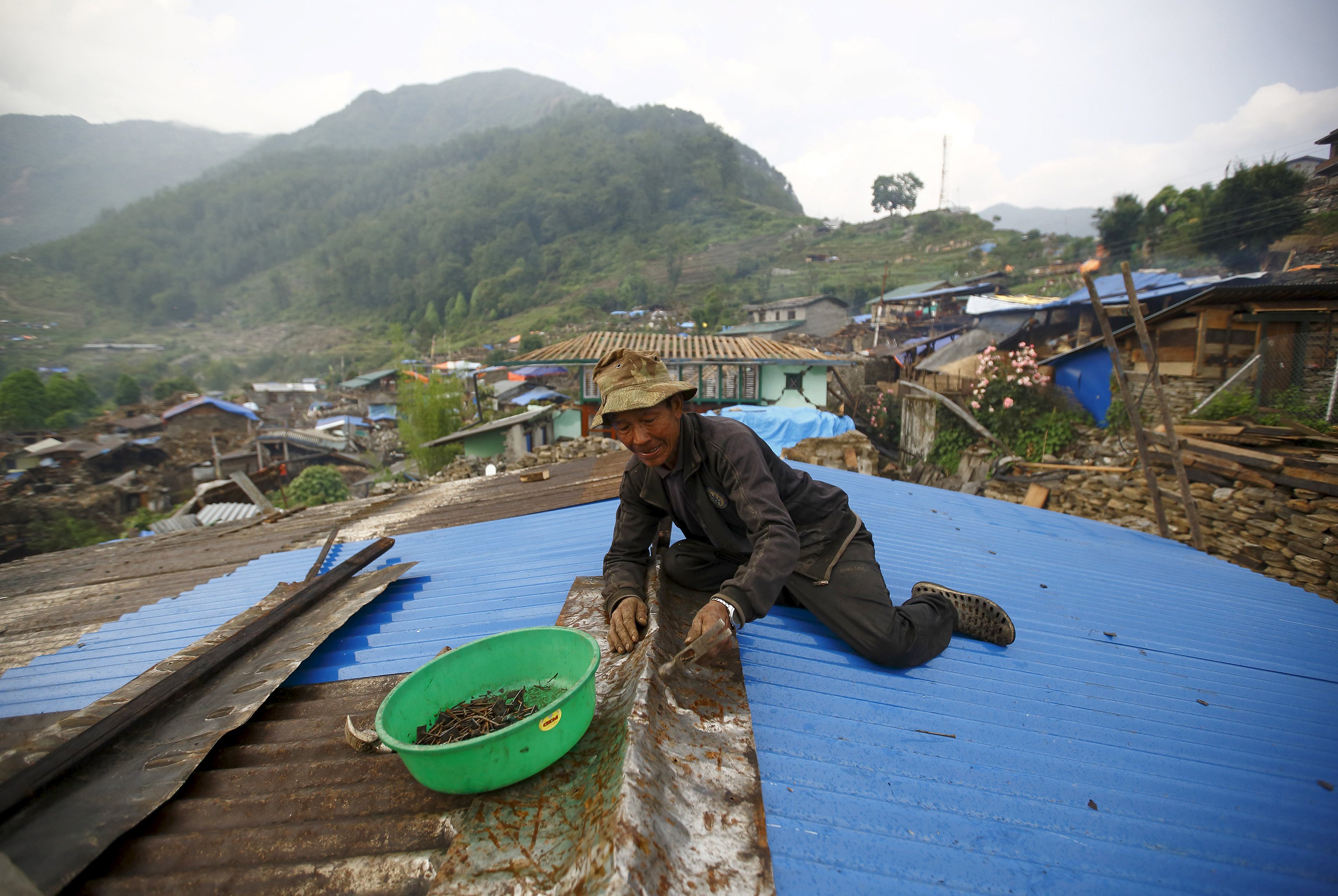 A man in Barpak village, in Nepal's Gorkha district, tries to repair the roof of his brother's house. Photo: Reuters