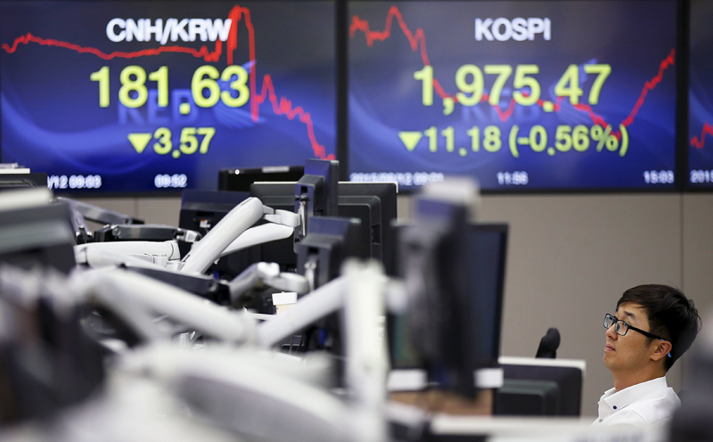 A currency dealer works in front of electronic boards showing the exchange rate between the Chinese yuan and South Korean won (left) and the Korea Composite Stock Price Index (KOSPI), at a dealing room of a bank in Seoul, South Korea, August 12, 2015. South Korea and other regional stock prices fell after China cut the value of its currency for the second day in a row. Photo: Reuters