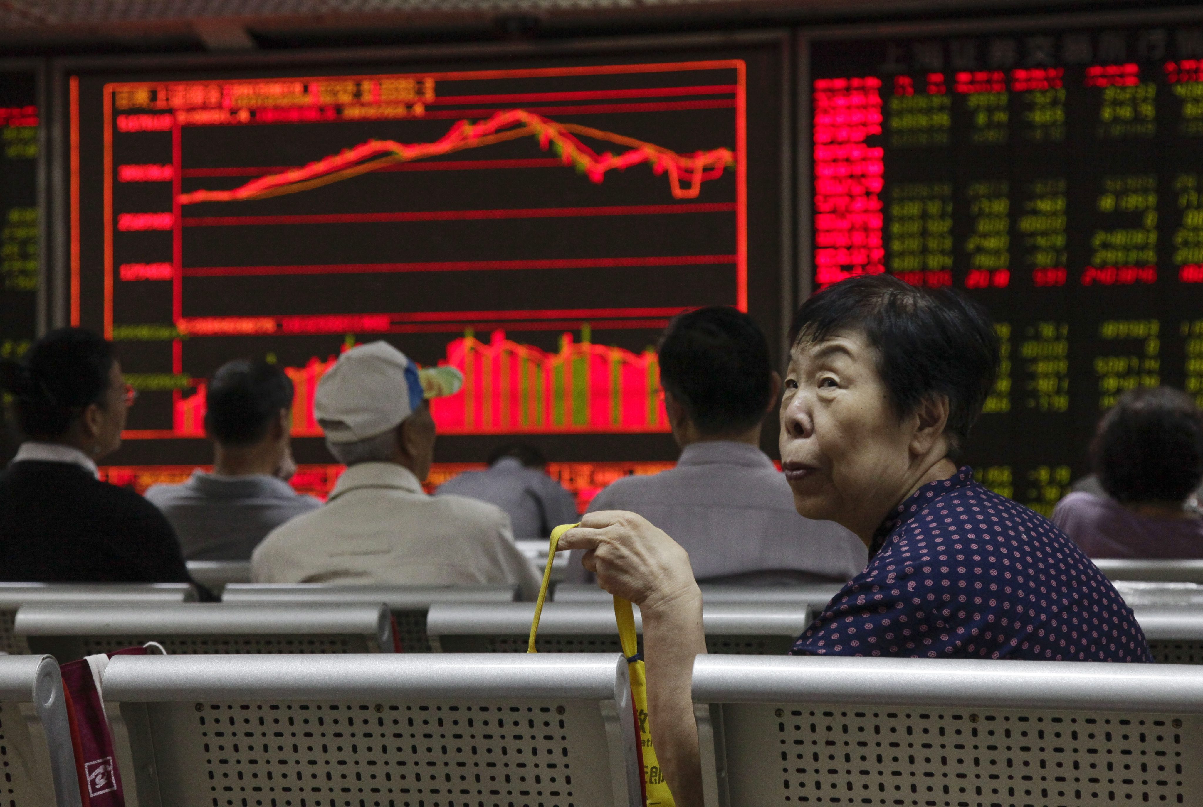 An investor looks up from her seat as stock data is displayed on an electronic board at a securities brokerage house in Beijing, China. Photo: EPA