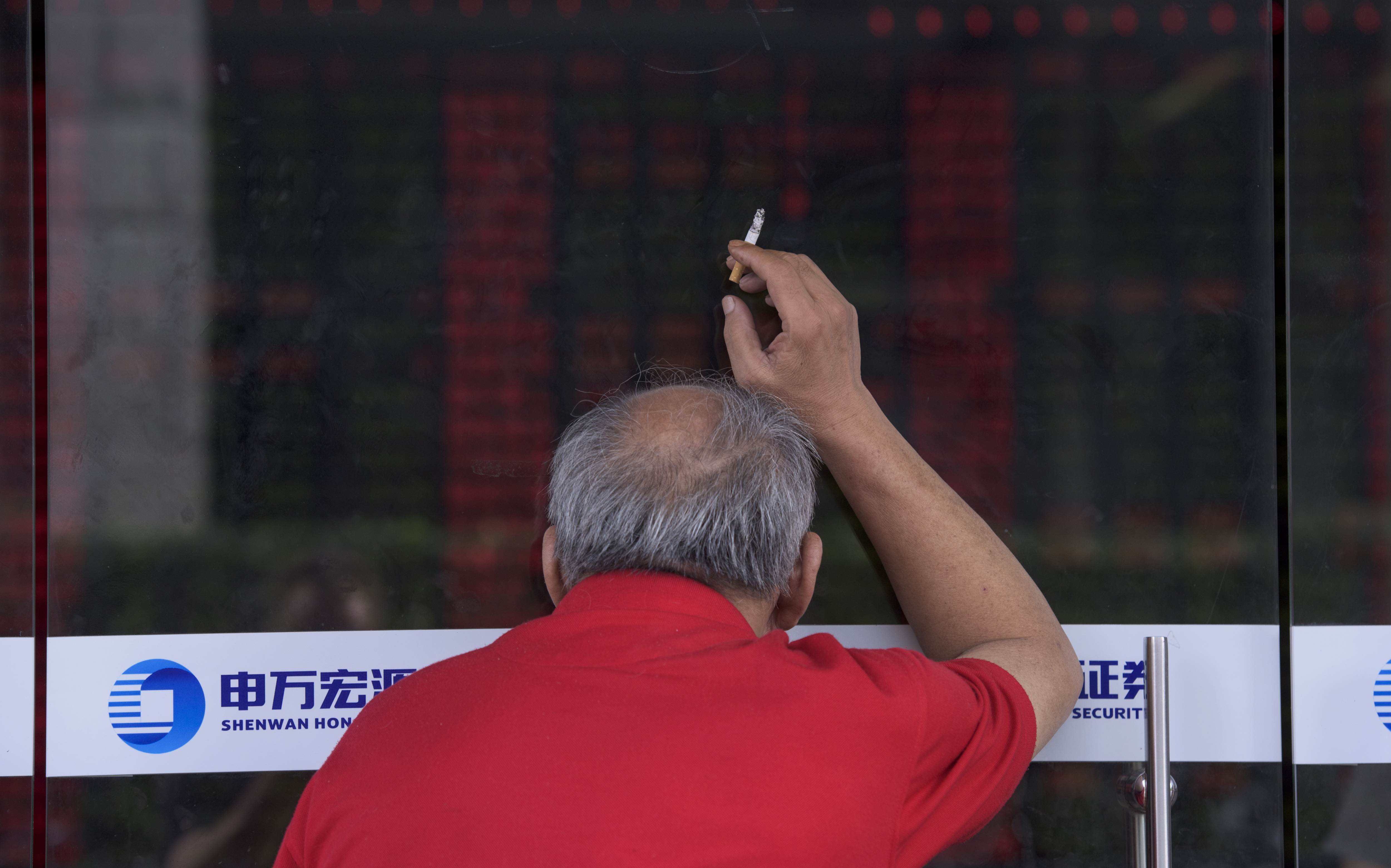 An investor holds a cigarette as he peers through a glass door to look at a digital board showing stock market movements at a brokerage house in Shanghai. Photo: AFP